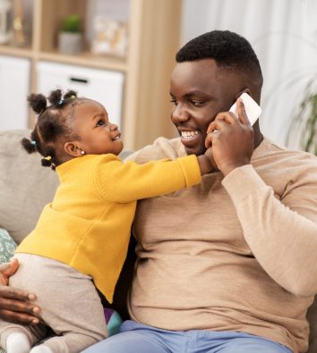family, fatherhood and technology concept - happy african american father with baby at home calling on smartphone